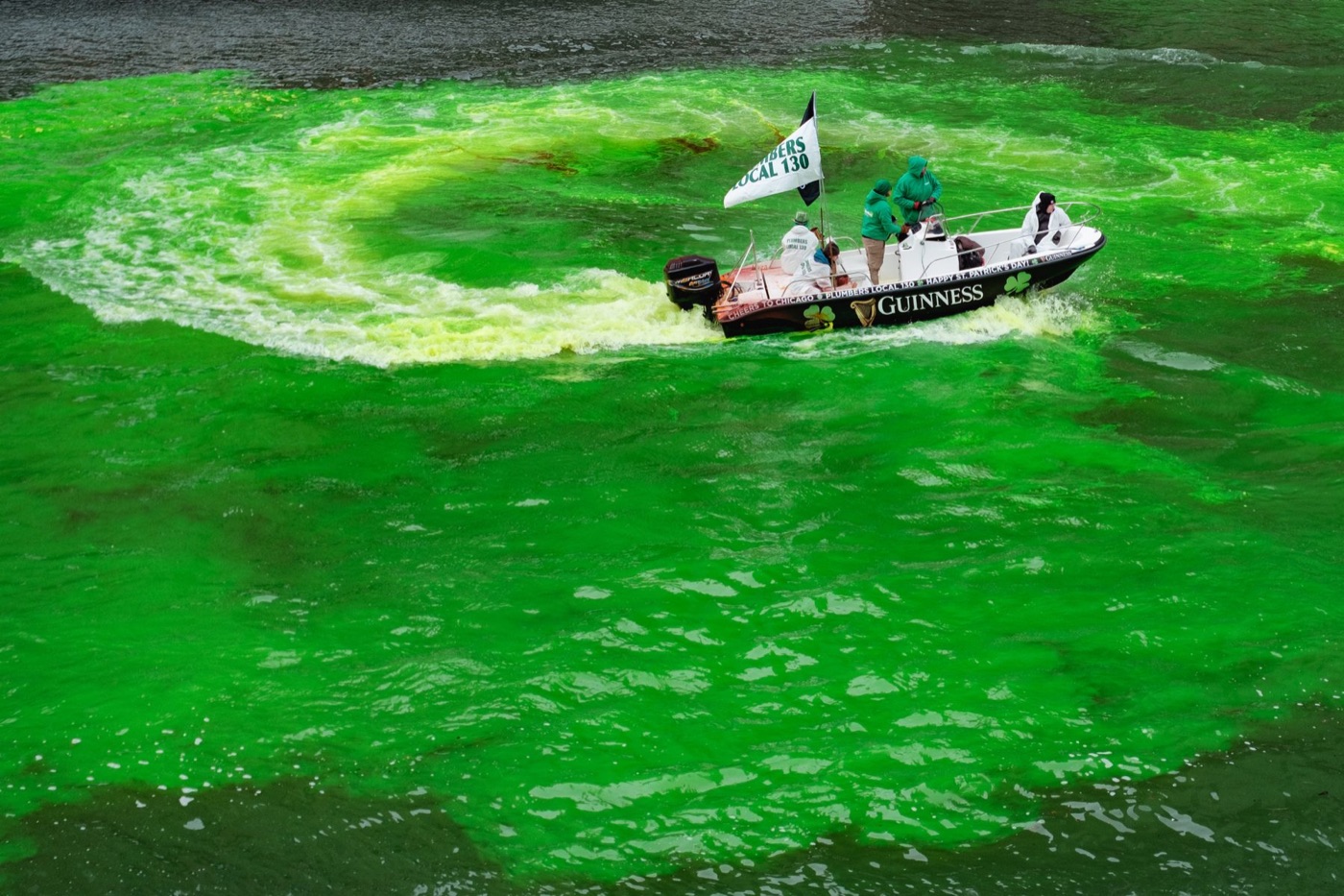 A boat tracing a wide curve through the Chicago River as it turns green for St. Patrick’s Day