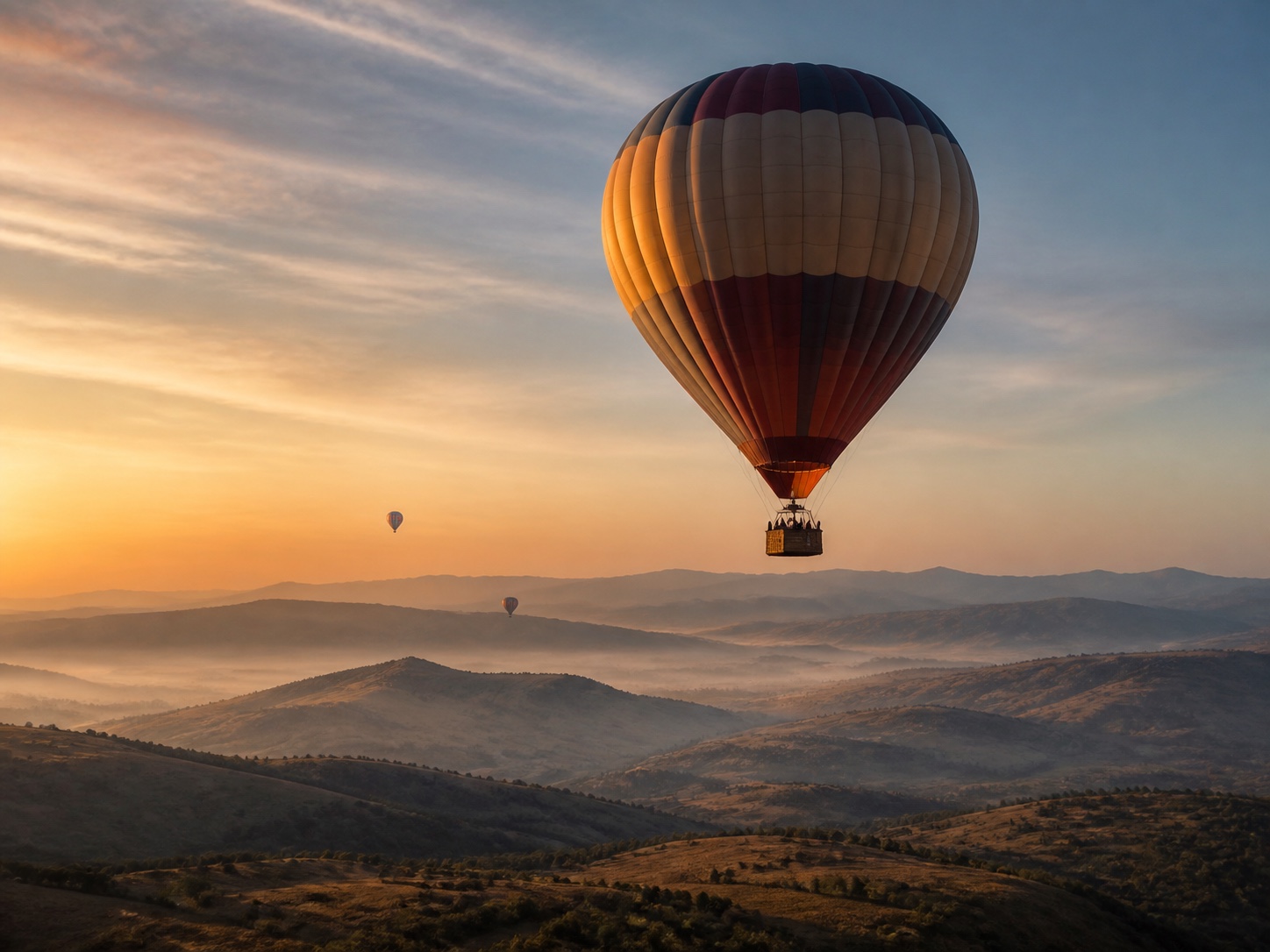 A hot-air balloon floating above a layered landscape at sunrise