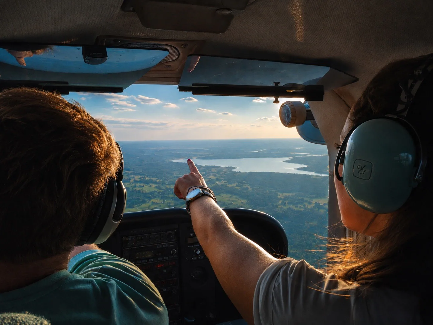 A man and woman wearing headsets in a small airplane over a lake at golden hour