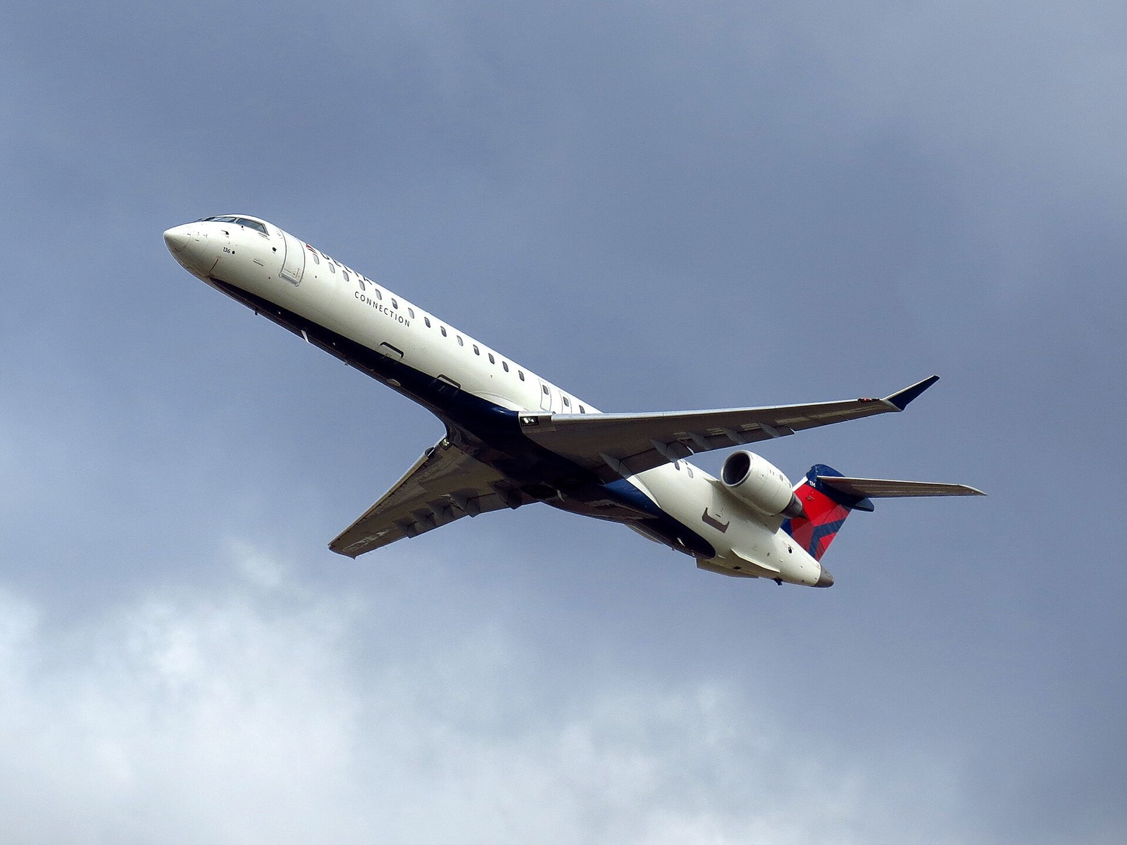 A Bombardier CRJ-900 climbing into a softly clouded sky