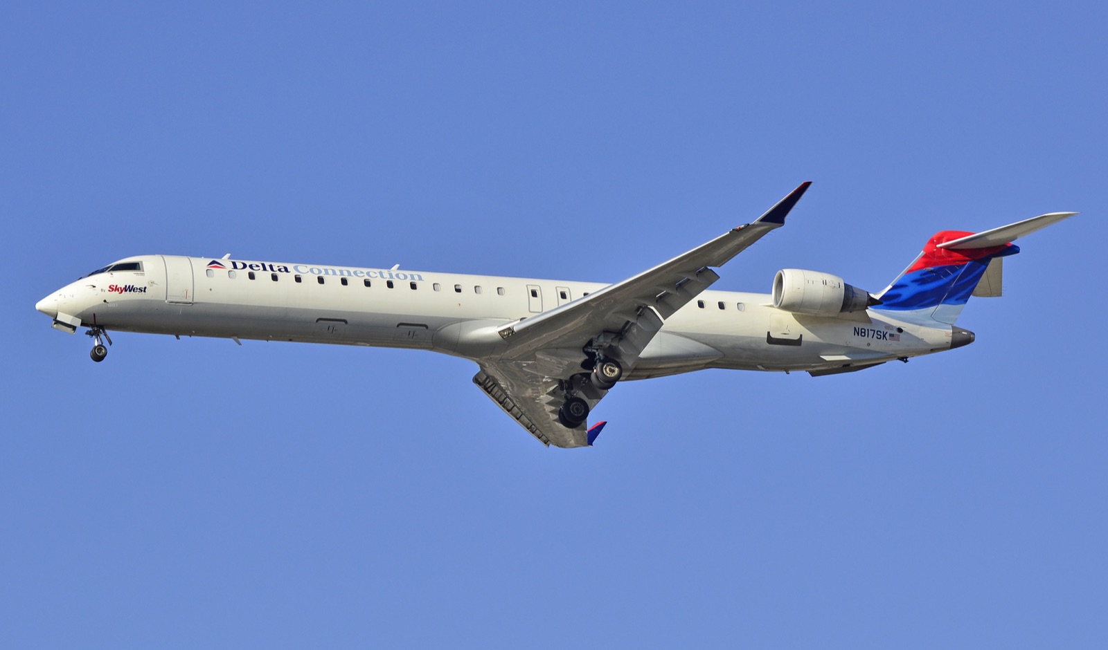A Bombardier CRJ-900 regional jet in flight against a clear blue sky